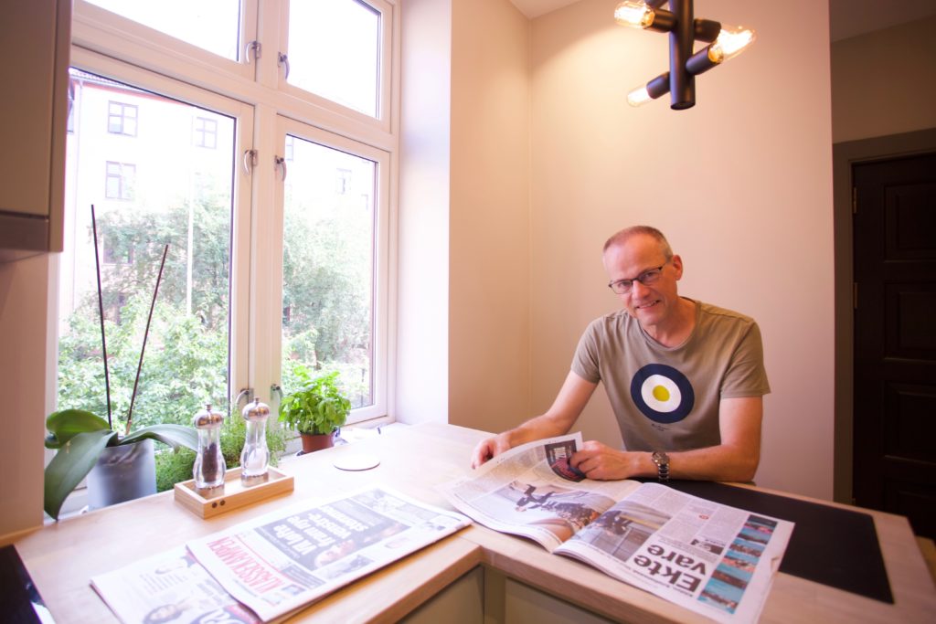Bilde av en mann som leser avisen ved kjøkkenbordet
